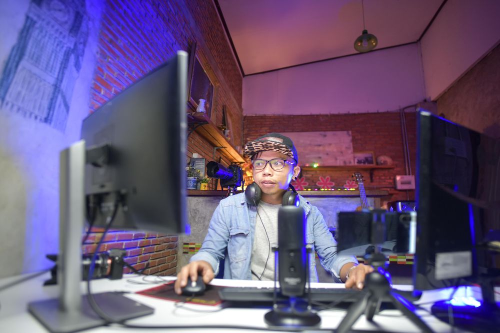 Man sitting beside microphone and two computer screens