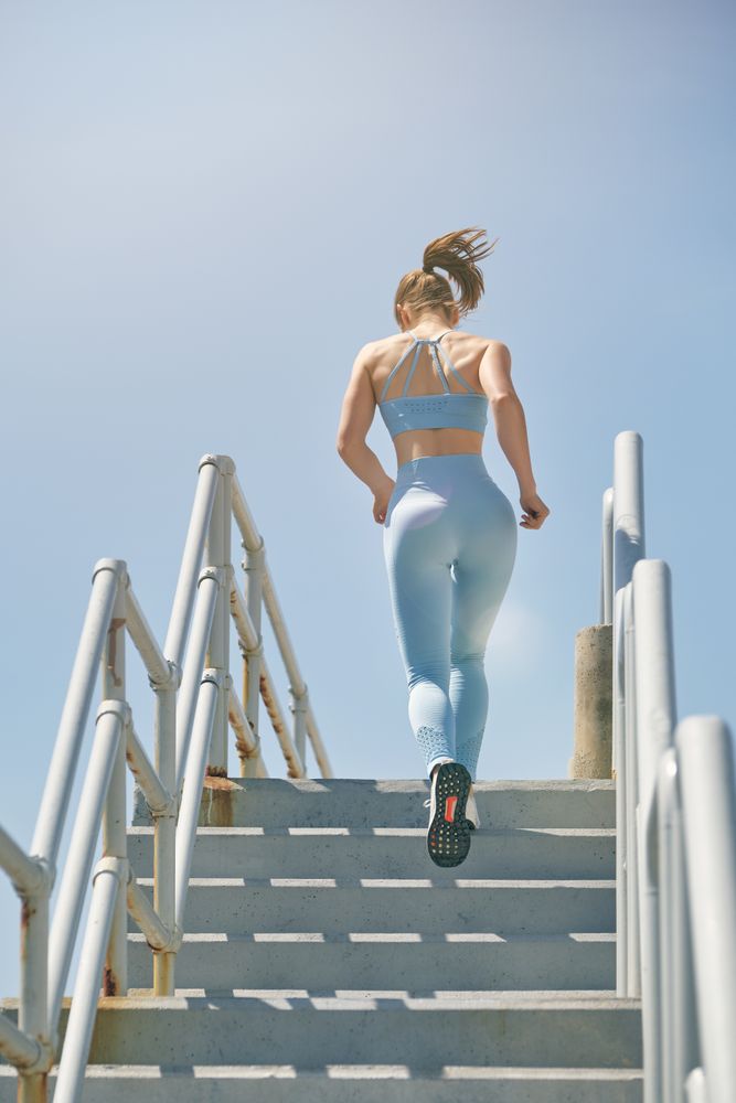Faceless athlete running on stairs in sunlight