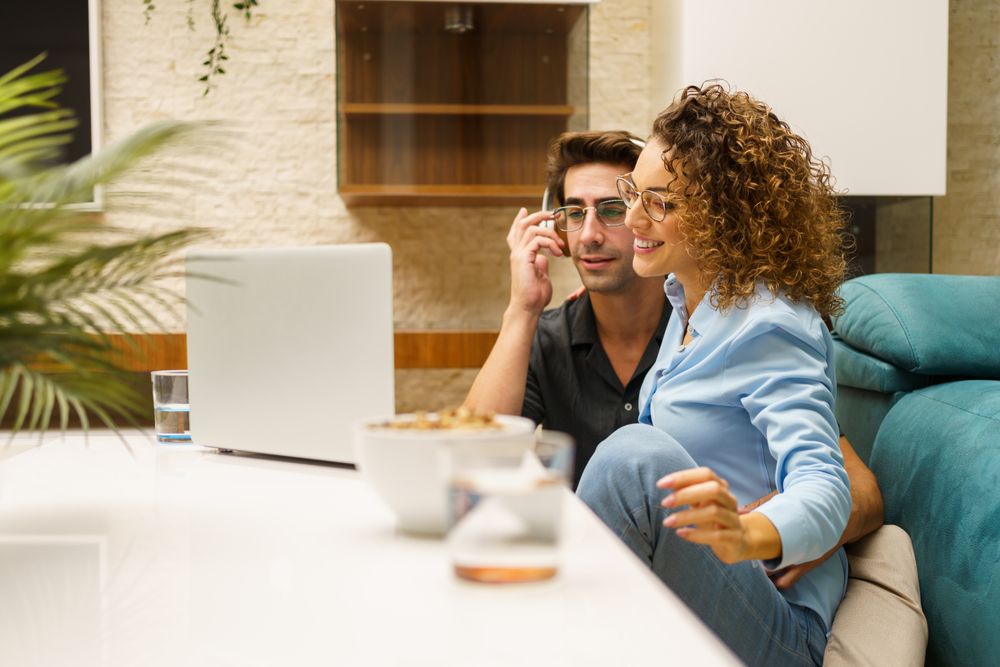 Cheerful couple sitting together in living room while using laptop