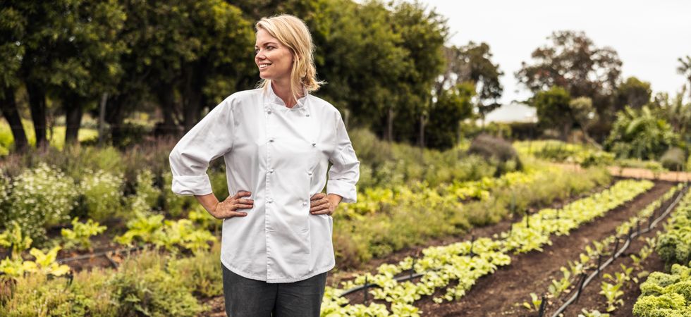 Happy female chef looking away thoughtfully while standing with her hands on her hips