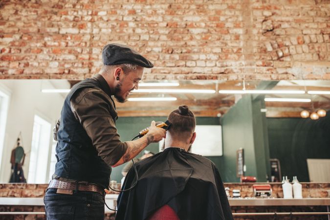 Barber trimming hair of client at salon with clippers