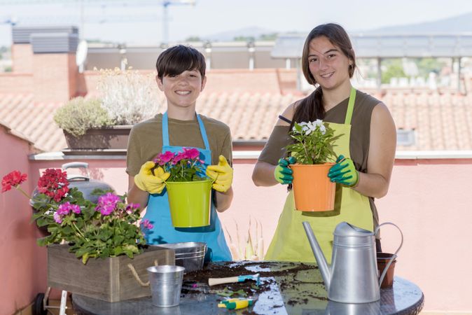 Two happy teenager wearing gardener apron posing with plants on balcony