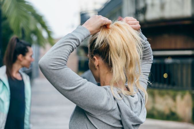 Back of blonde woman runner tying her hair in a ponytail before training