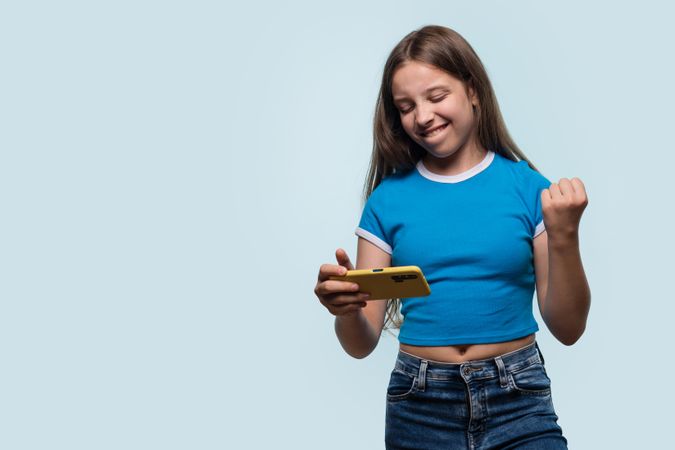 Girl clenching fist in triumph while looking at smartphone.