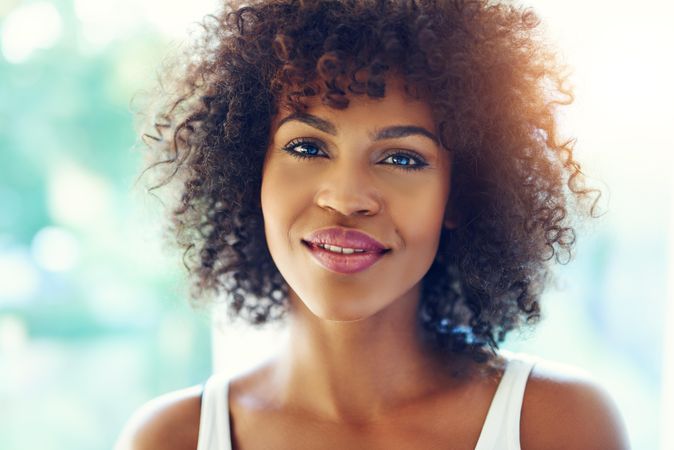 Female with curly hair looking at camera and half smiling on blurry leafy background