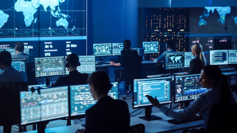 Professionals Analyze Cybersecurity Data in a Futuristic Control Room, Surrounded by Multiple Screens Displaying Global Metrics. the Collaborative Environment Fosters Innovative Solutions and Strategic Insights.