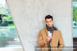 Man in fall coat texting while leaning back on cement pillar 5aXKxo
