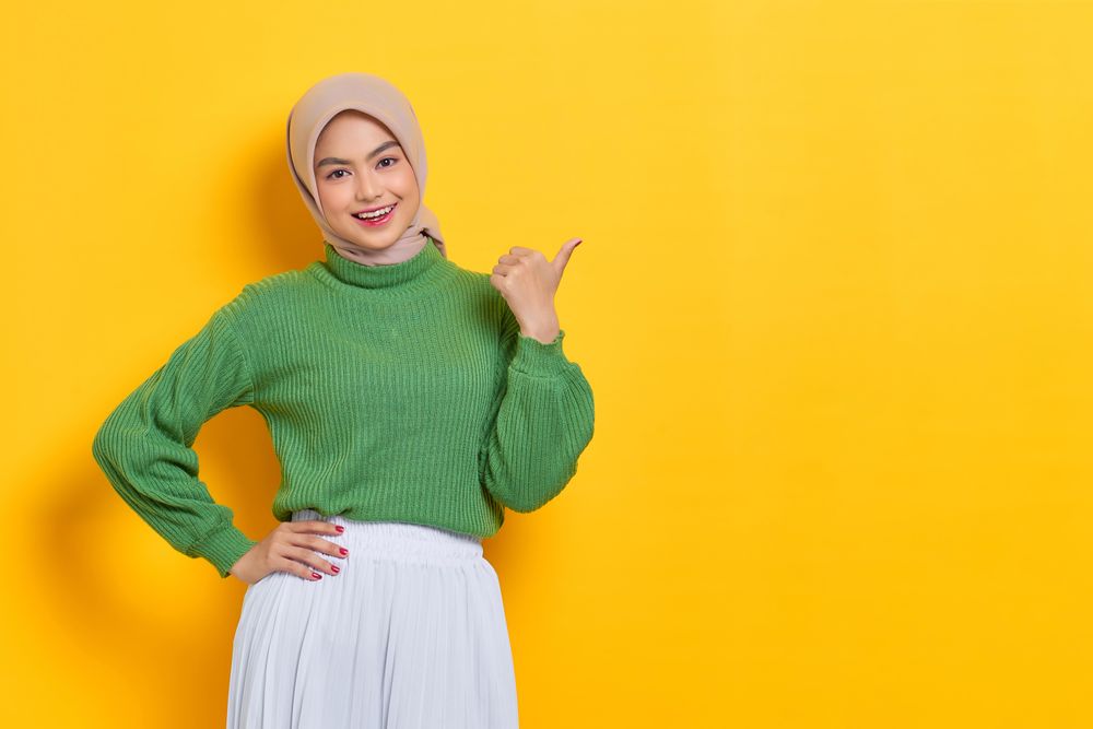 Smiling woman in headscarf pointing her thumb to the side