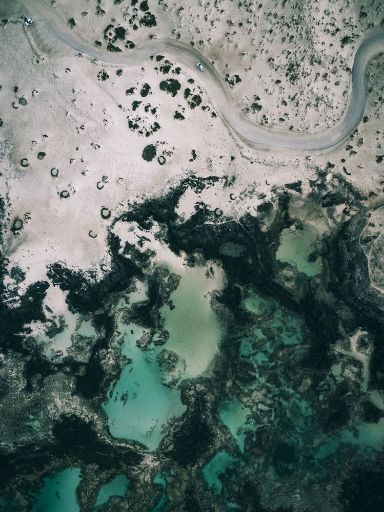 Aerial shot of a winding road in the sand next to the coast