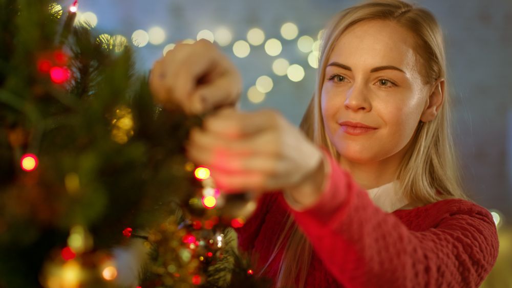 Woman Decorates Christmas Tree with Ball Ornament.
