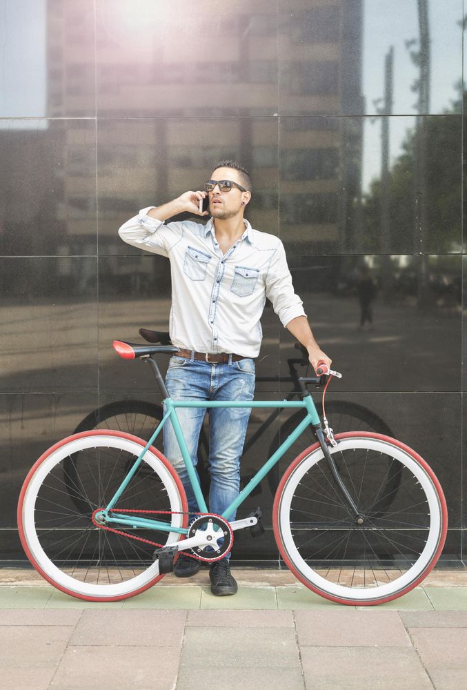 Male standing with his bike next to reflective wall having conversation on phone