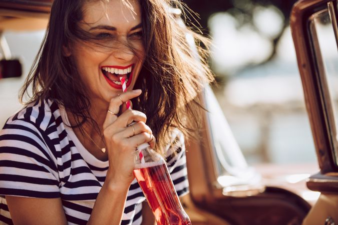 Female on a road trip having soft drink while laughing