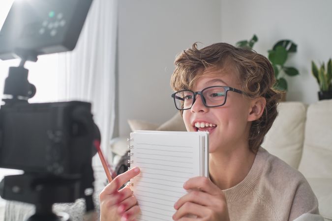 Smart positive boy in glasses recording video on camera at home