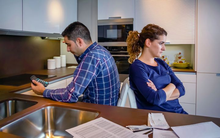 Couple with their backs to each other in kitchen with bills on counter