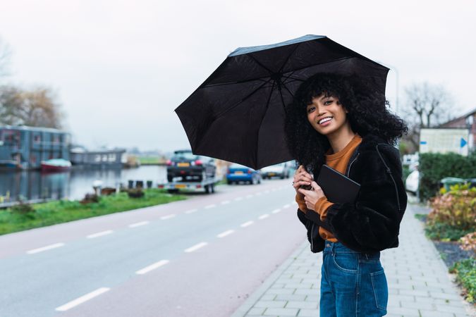 Smiling Black woman with umbrella on street
