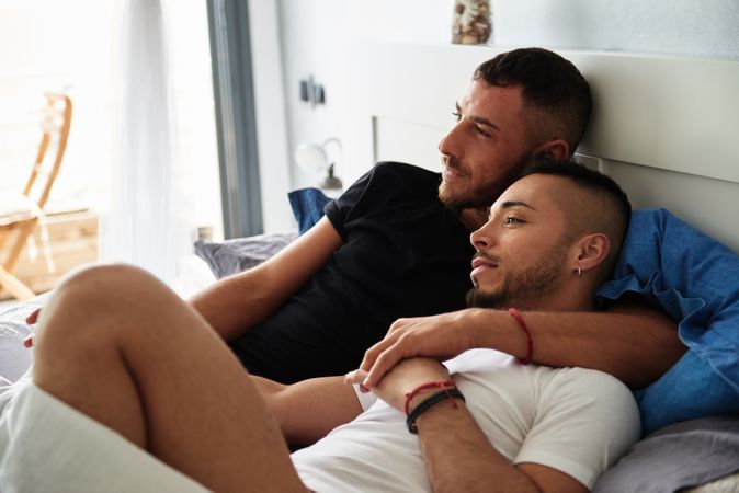 Smiling gay couple hugging on bed