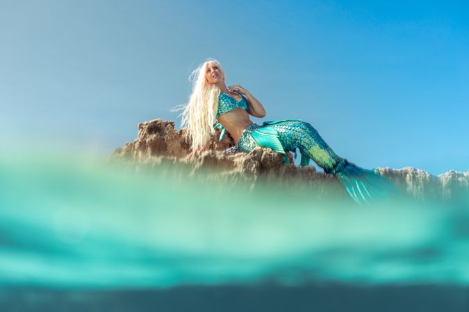 Blond fairytale female mermaid lying on rock