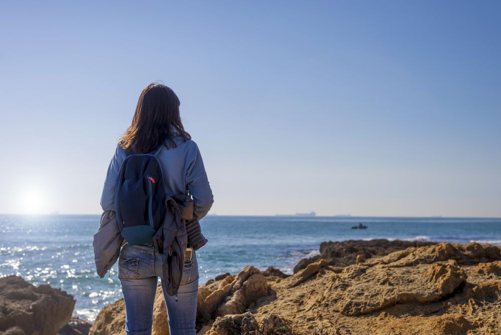 Woman looking out at sea from rocky shore