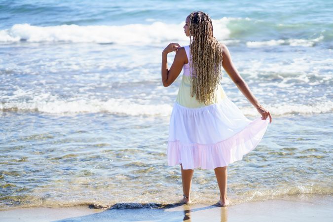 Barefoot Black woman walking along the shore in colorful dress