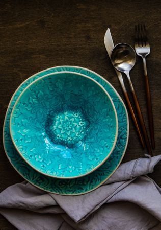 Rustic table setting of patterned teal bowl with cutlery