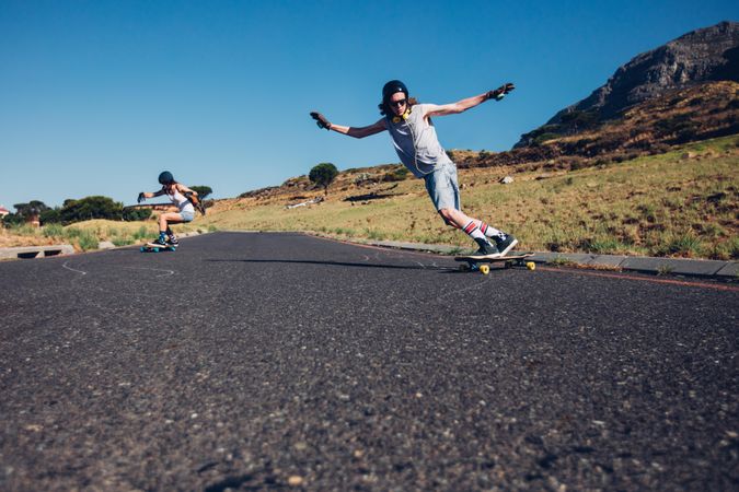 Young man and woman skateboarding on the rural road