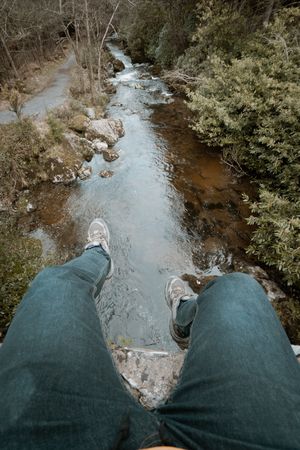 Tourist sitting on bridge and dangling legs over river