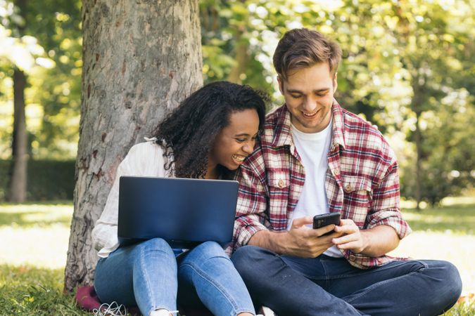 Multiracial couple studying in the park with laptop