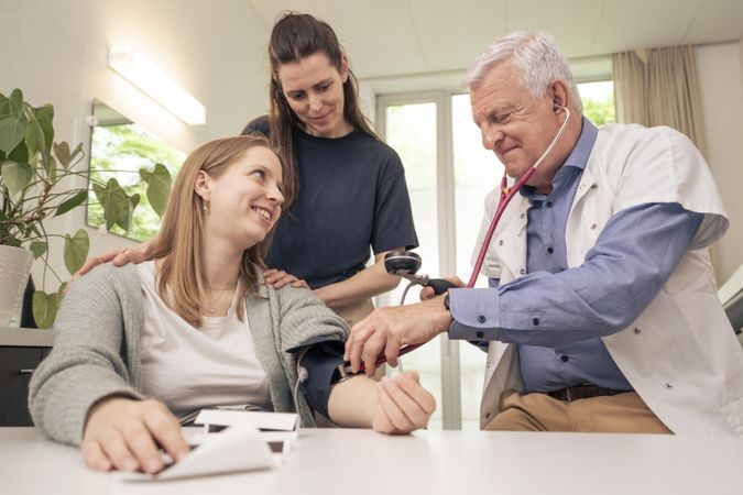 Doctor checking pregnant woman's blood pressure as her partner comforts her.