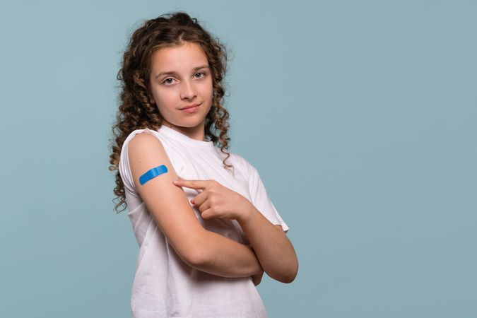 Girl pointing at blue bandage after receiving vaccination.