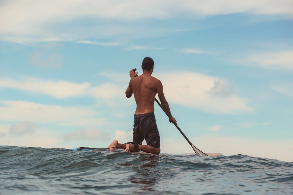 Man with paddle on surf board waving on water