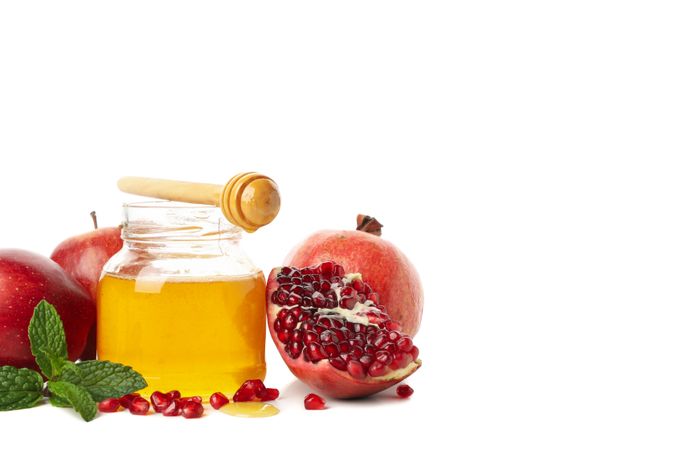 Pot of honey with dipper, open pomegranate and apples on left with copy space