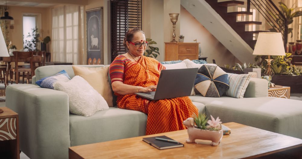 Mature Indian Woman Using Laptop at Home: Enhancing Her Culinary Skills with Online Cooking Classes, Exploring New Recipes, Sharing Family Traditions.