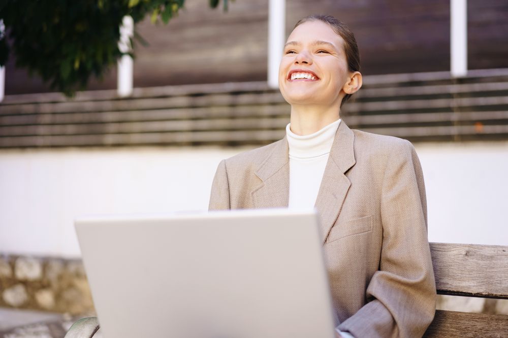 A Smiling Businesswoman is Enjoying Her Work on a Laptop While Sitting Outdoors in Nature