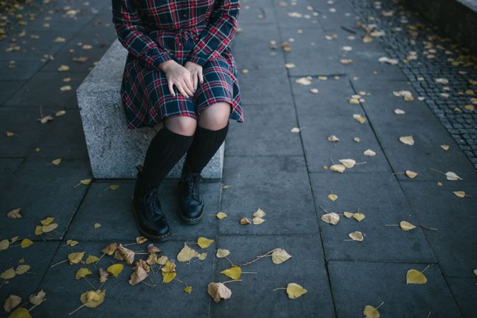 Woman in dress and dark boots sitting on gray concrete bench