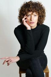 Woman dressed in dark sweater and looking at camera resting head on hand