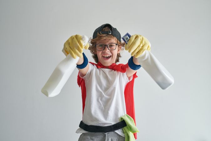Joyful boy in housekeeper costume standing with detergent bottle