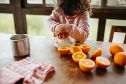 Small girl squeezing oranges on reamer to make juice