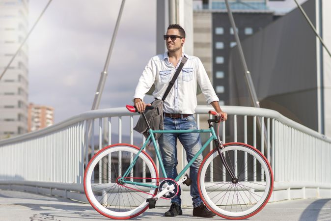 Male with bicycle on bridge with city in background