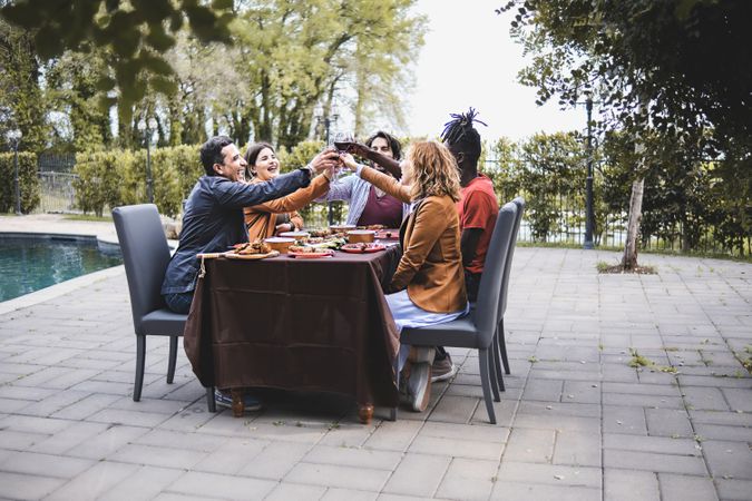 A diverse group of friends cheerfully toasting with drinks at an outdoor party around the table