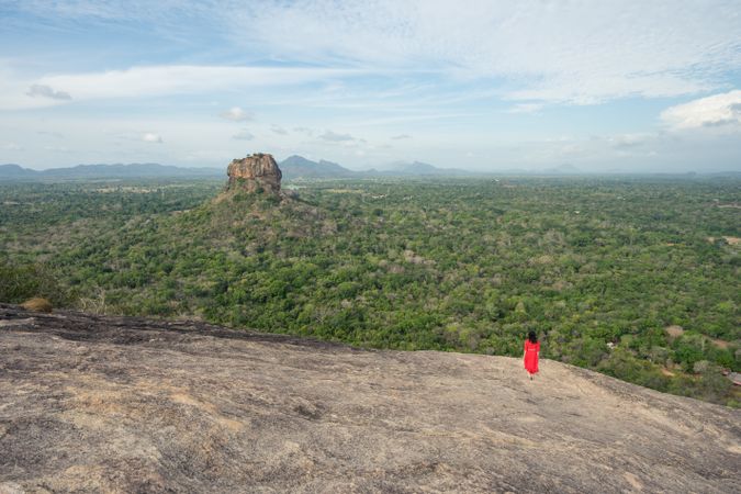 Tourist against solitary rock in middle of green forested plain under clear sky in summer