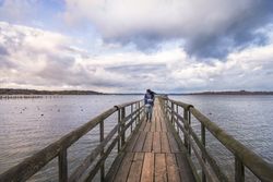 Woman walking on bridge over calm lake at sunset