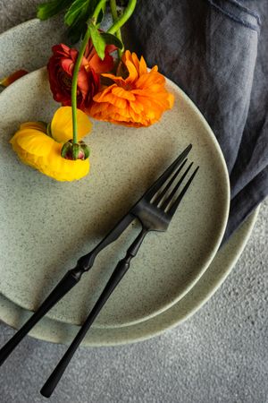Rustic table setting with ranunculus flowers on grey plate, vertical composition