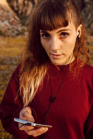 Young woman with piercing listening music on smartphone on hill