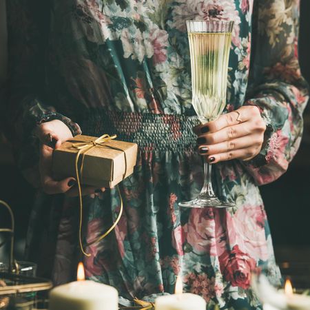 Woman in floral dress holding small box with a bow, and flute of champagne