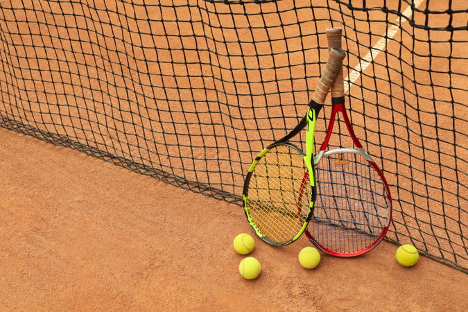 Rackets and tennis balls against net on clay court