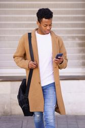 Content Cuban male walking outside holding his phone, vertical