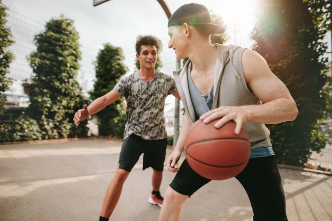 Two young friends playing basketball on court outdoors