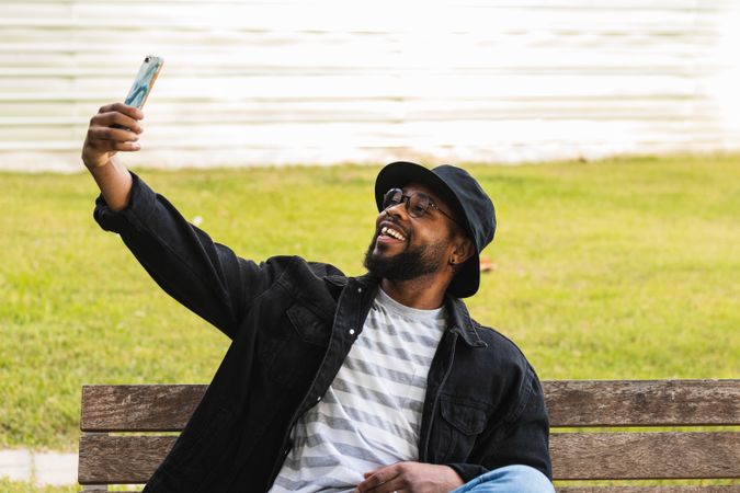 Trendy Black man taking selfie on bench