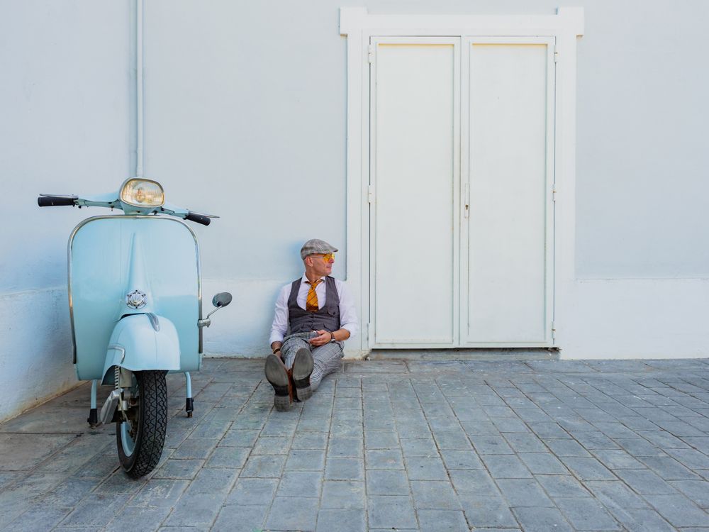 Trendy man sitting on floor near vintage scooter