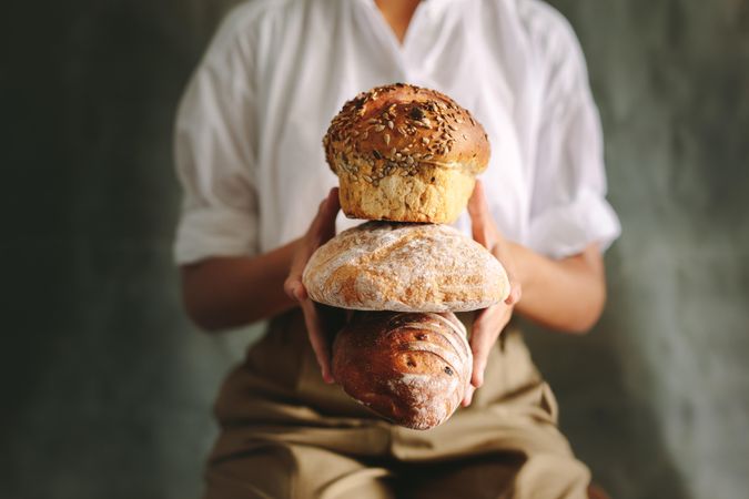 Cropped shot of chef holding various types of loaf bread against gray background